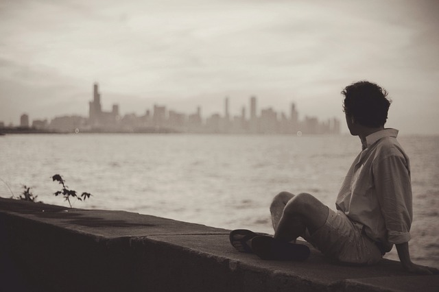 man sitting at the quay looking at the city far away